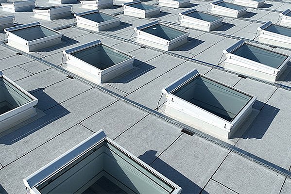 Regelmäßiges Gitter aus rechteckig eingebauten Flachdachfenstern auf grauem Flachdach