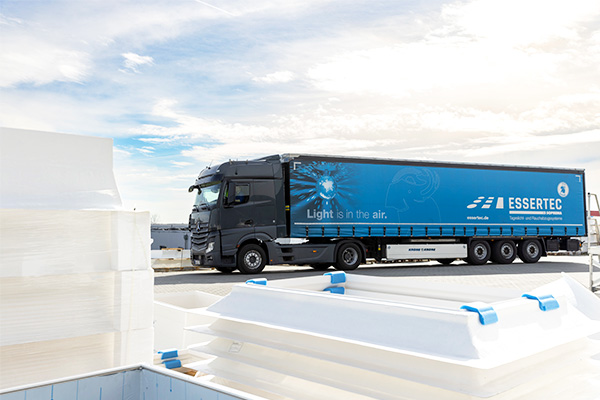 ESSERTEC-LKW mit blauer Plane, Aufschrift "Light is in the air", im Vordergrund Produktstapel